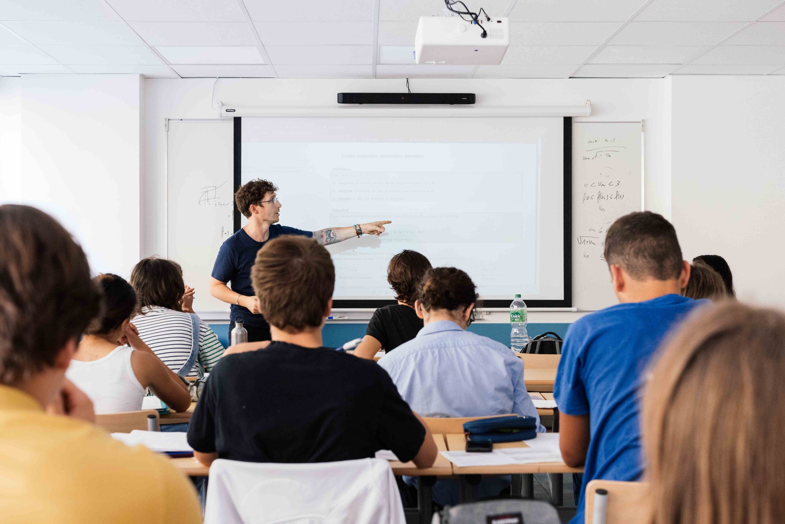 Enseignant donnant un cours devant un tableau interactif à une classe d’étudiants attentifs en classe prépa scientifique, dans une salle de cours lumineuse du lycée privé Michelet à Nice.