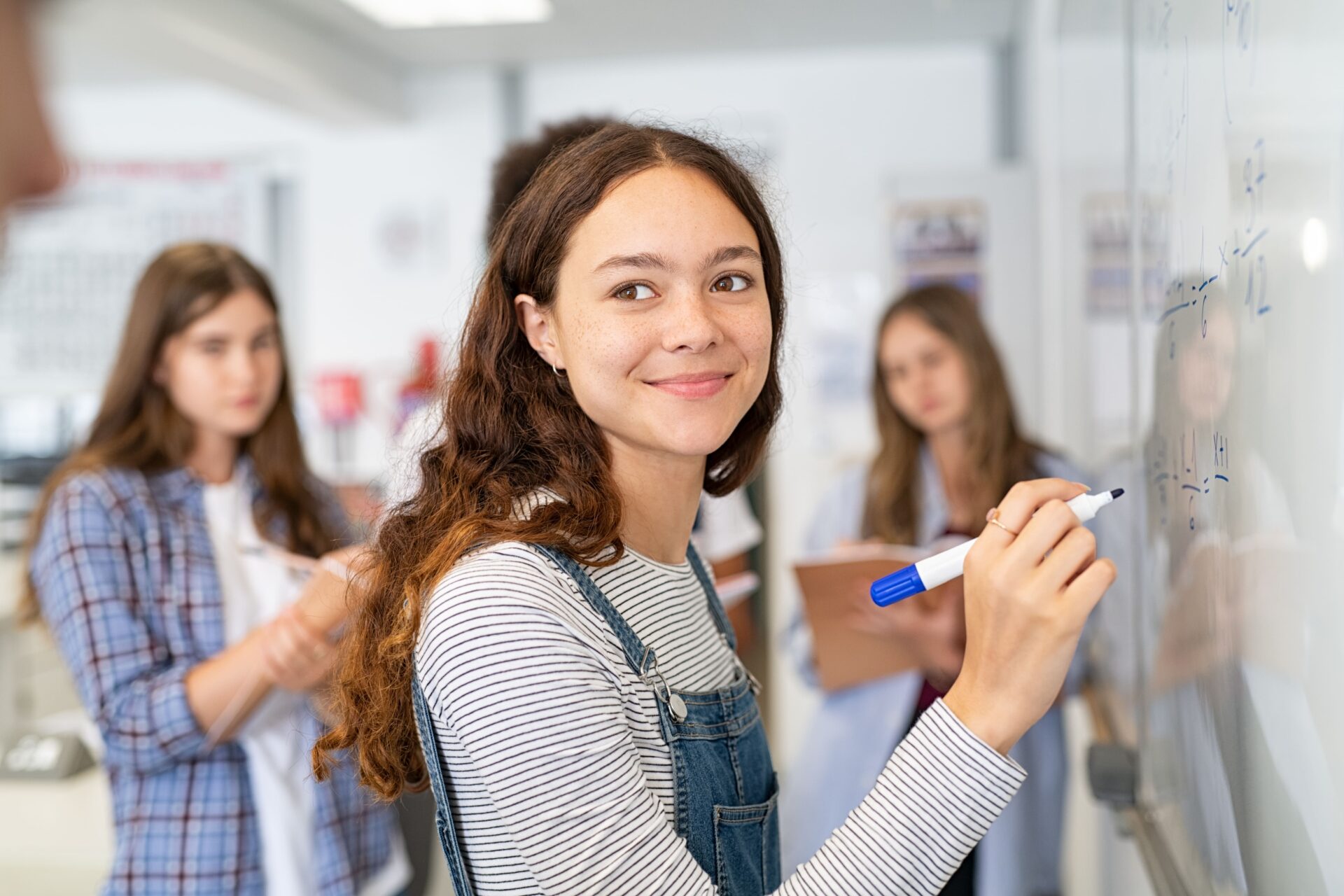 Une jeune étudiante qui écrit sur un tableau durant un cours de mathématiques.